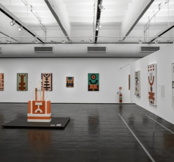 Image of museum exhibit featuring sculpture and prints of abstract art in mostly orange and turquoise colors