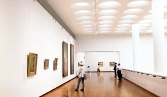 Image of a few people looking at paintings inside the museum